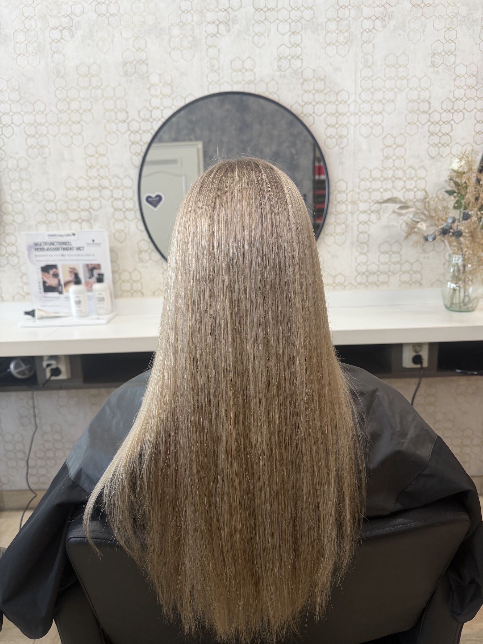 Lang, sluik blond haar na de behandeling, gezien vanaf de rug bij de spiegel